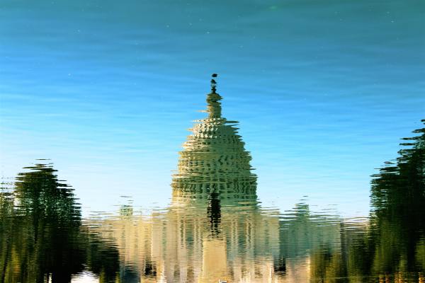 a rippled reflection in a puddle of a domed congressional building against a clear blue sky