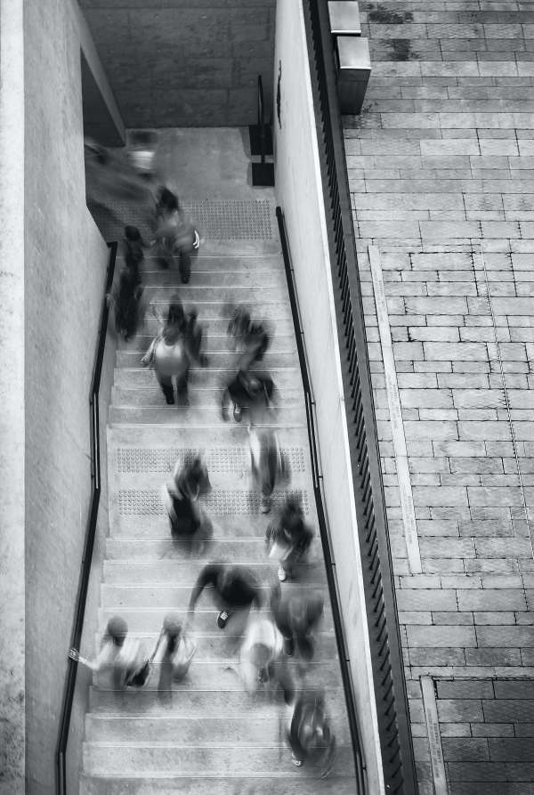a black and white image of people descending and ascending a staircase. The subjects are blurred indicating fast movement